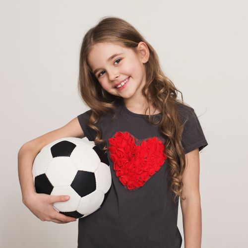 A little girl in a heart shirt holds a soccer ball