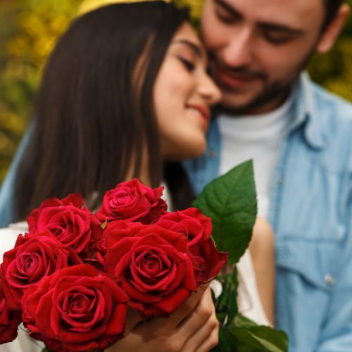 A man and woman embrace while holding red roses