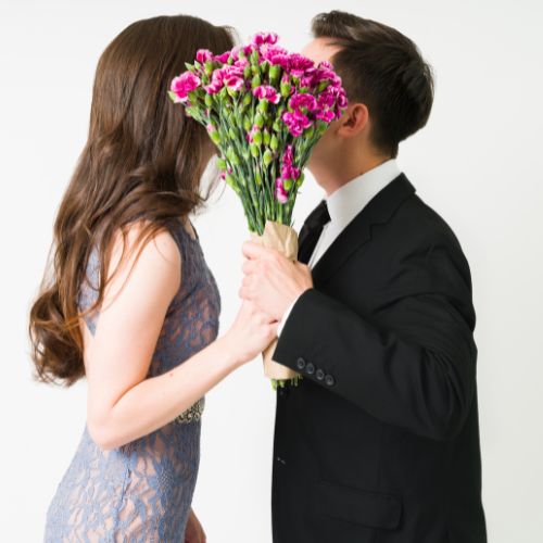 A man and woman kiss while holding a bouquet of flowers