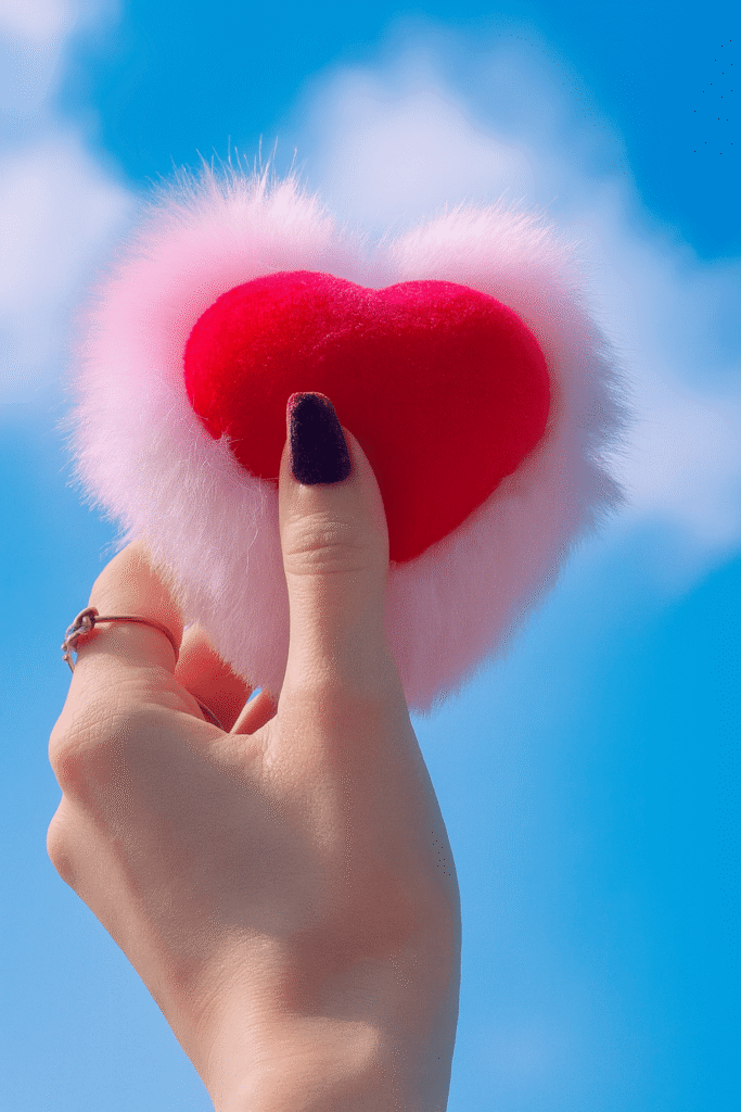 A person holds a heart-shaped object against a clear blue sky backdrop