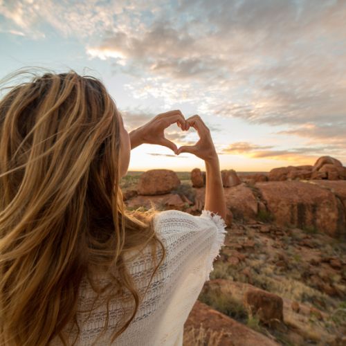 A woman forms a heart shape with her hands against a vast desert backdrop