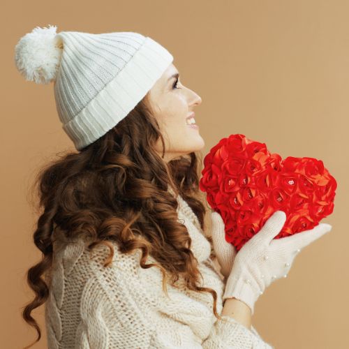 A woman wearing a white hat and gloves holds a red heart