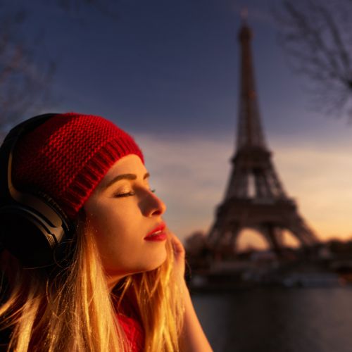 A woman with headphones enjoys music while sitting near the Eiffel Tower