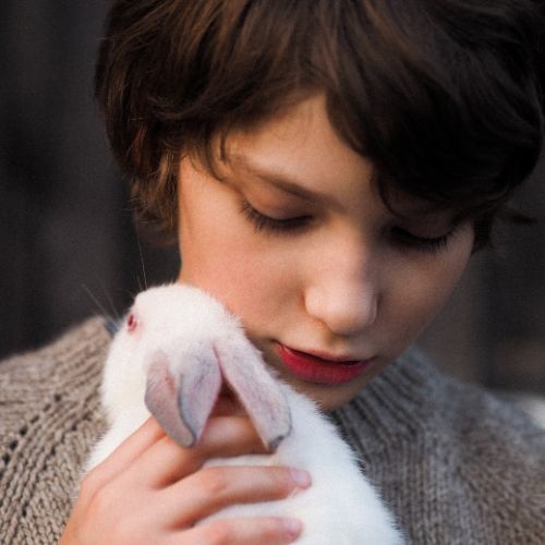 A young boy smiles while holding a fluffy white rabbit in his arms