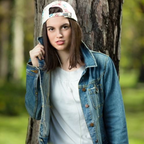 A young woman in a hat and denim jacket smiles at the camera