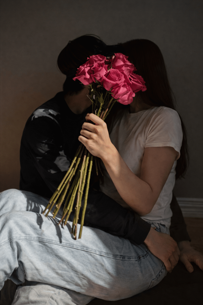 A man and woman kiss while holding a bouquet of roses