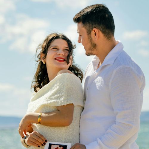 A pregnant woman and a man stand together on the beach